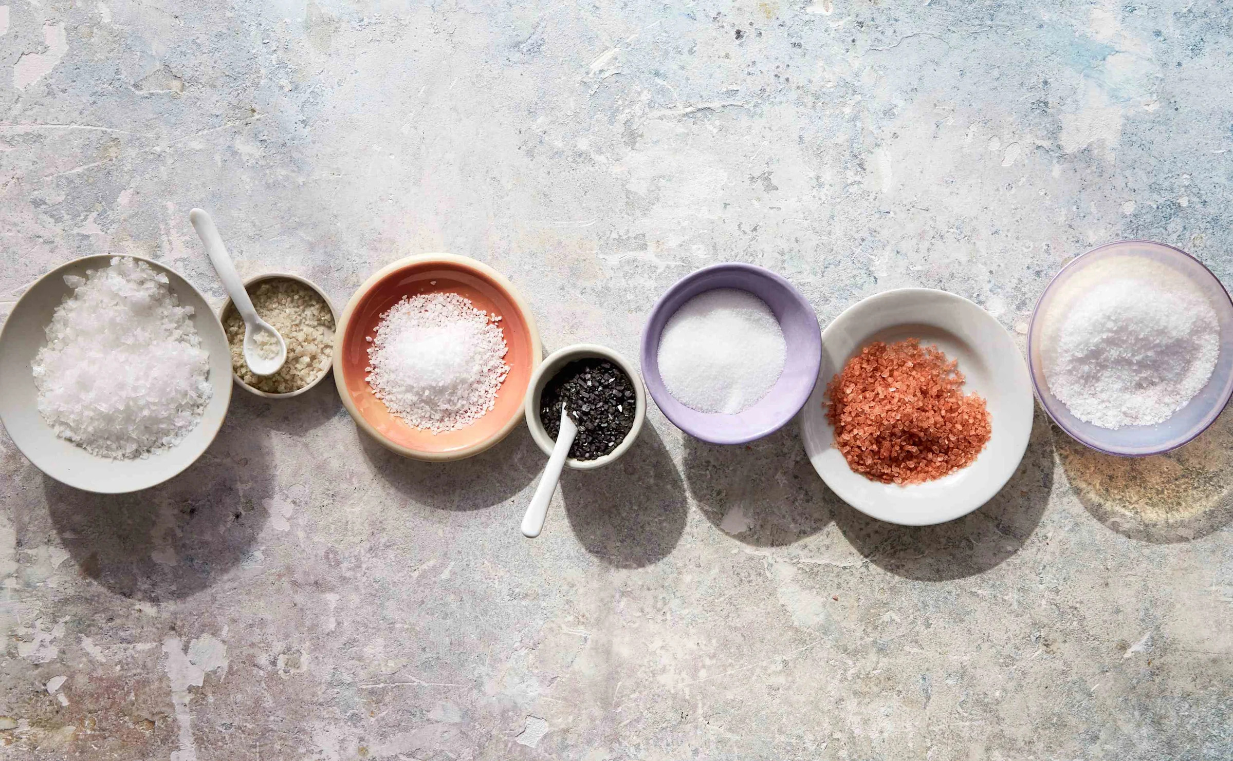 Three bowls of different salts on a wooden surface